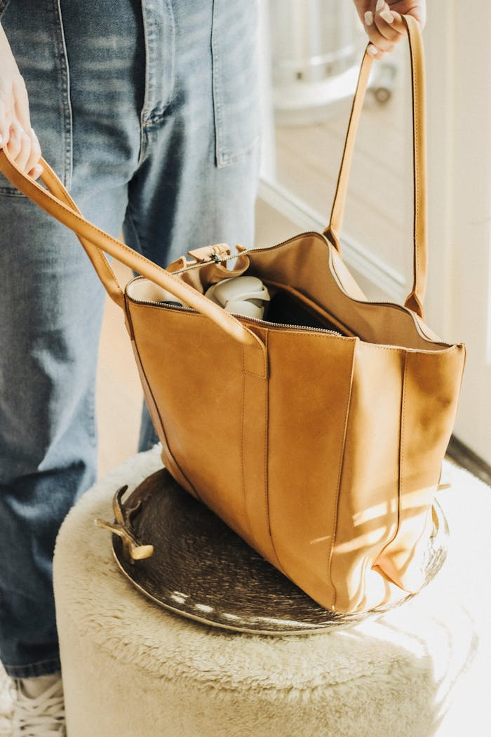 Stylish tan leather tote bag with accessories, perfect for travel and fashion enthusiasts.